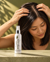 Load image into Gallery viewer, Woman parting her straight black hair at the crown beside a Bio Follicle Normal spray bottle